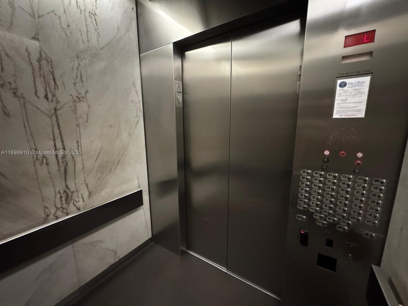 An elevator interior features stainless steel doors, a metal control panel, and marble-patterned wall panels — 1040 Biscayne Blvd # 1106, Miami FL 33132, MIAMI, FL