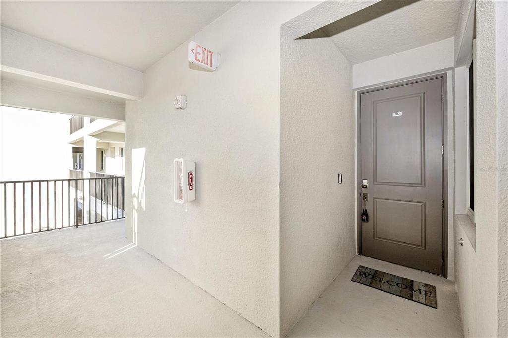 An exterior apartment hallway features a grey door, a fire extinguisher cabinet, and metal railings — 12240 WELLEN GOLF STREET UNIT 207, VENICE, FL