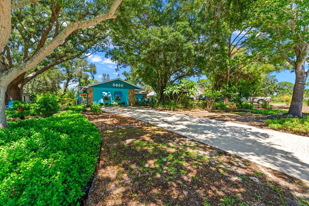 A bright blue house with a long concrete driveway sits under large, leafy oak trees — 2159 BARCELONA WAY, ST PETERSBURG, FL