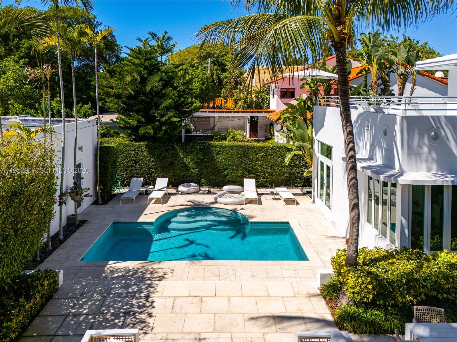 An outdoor swimming pool is surrounded by a stone patio, lounge chairs, and lush landscaping — 4580 Post Ave, Miami Beach FL 33140, MIAMI BEACH, FL