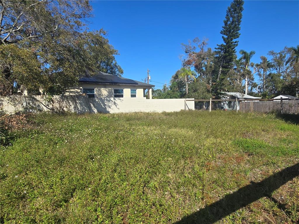 A vacant, grassy lot sits in front of a house with a beige wall — 1756 DR MARTIN LUTHER KING JR STREET S, ST PETERSBURG, FL