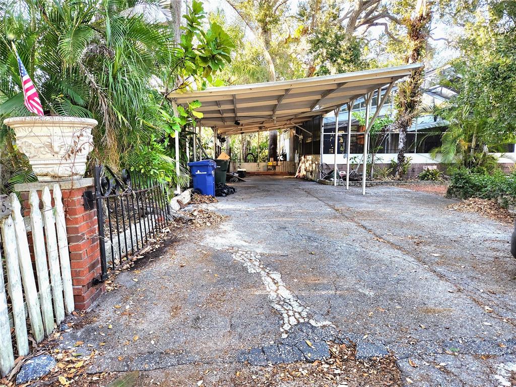 A paved driveway leads to a metal carport beside a house with a white fence — 286 SHAMROCK DRIVE, VENICE, FL