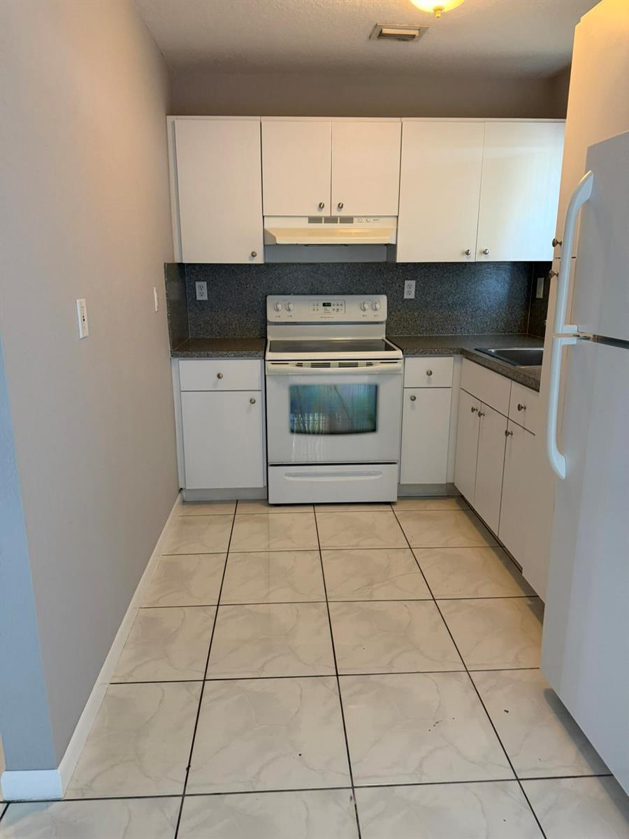 A galley kitchen features white cabinets, a white stove, and light-colored tile flooring — 661 S Biscayne River Drive, Miami FL 33169, MIAMI, FL
