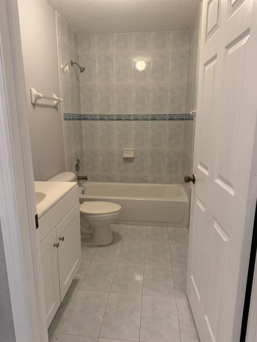 A small bathroom features a white vanity, a toilet, and a tiled tub-shower combination — 661 S Biscayne River Drive, Miami FL 33169, MIAMI, FL