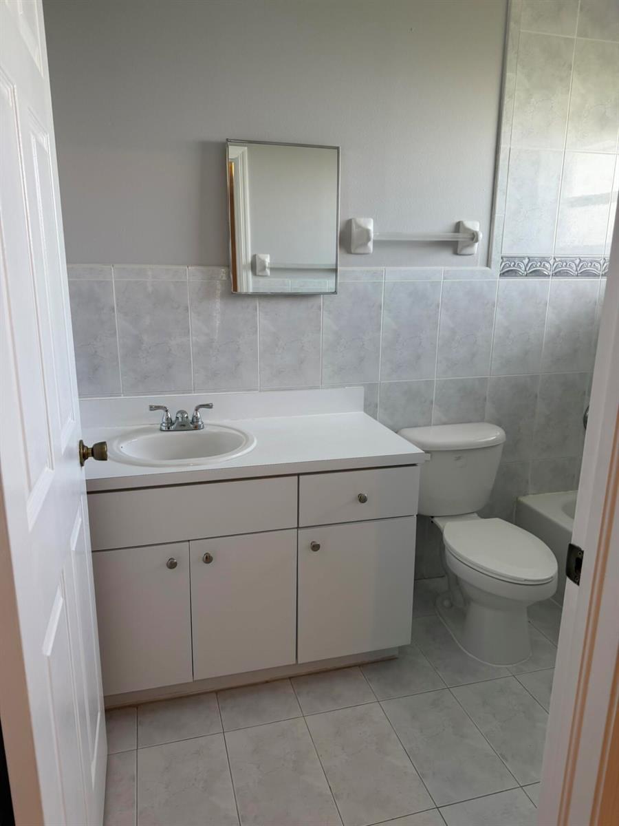 A bathroom features a white vanity, a toilet, and light-colored tile walls and flooring — 661 S Biscayne River Drive, Miami FL 33169, MIAMI, FL