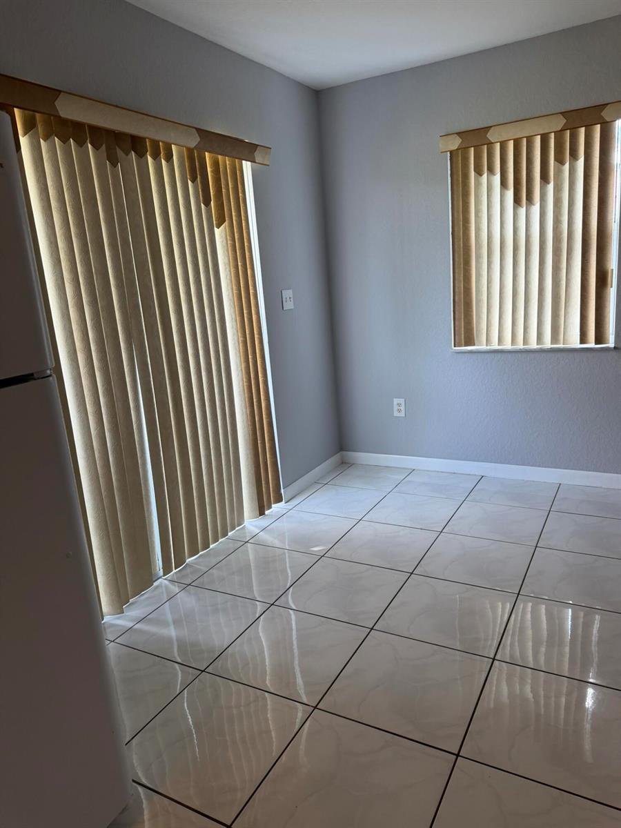 A room with light gray walls, white tile flooring, vertical blinds, and a sliding glass door — 661 S Biscayne River Drive, Miami FL 33169, MIAMI, FL