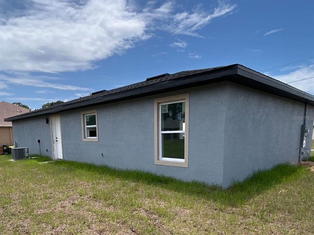The exterior of a gray stucco house features a dark roof and two white-framed windows — 3908 EL RADO AVENUE, SEBRING, FL