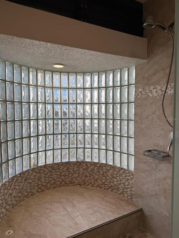 A walk-in shower features a curved glass block wall, beige tile flooring, and stone walls — 702 PISOS DE MIRAMAR, SAN JUAN, PR