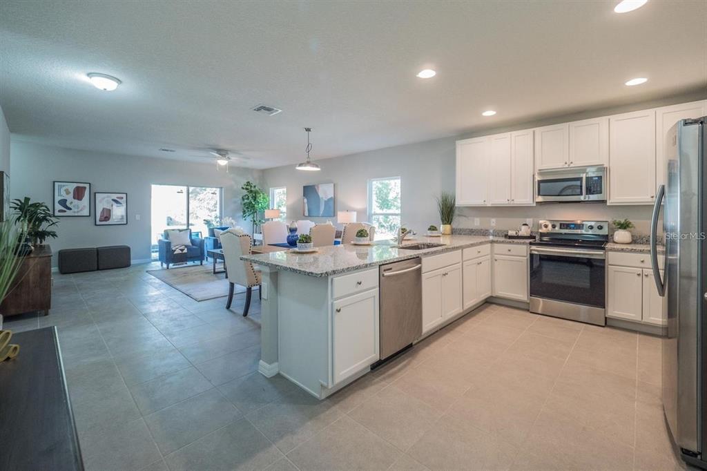An open-concept kitchen with white cabinets and granite countertops overlooks a dining and living area — 248 CHESHIRE COURT, KISSIMMEE, FL