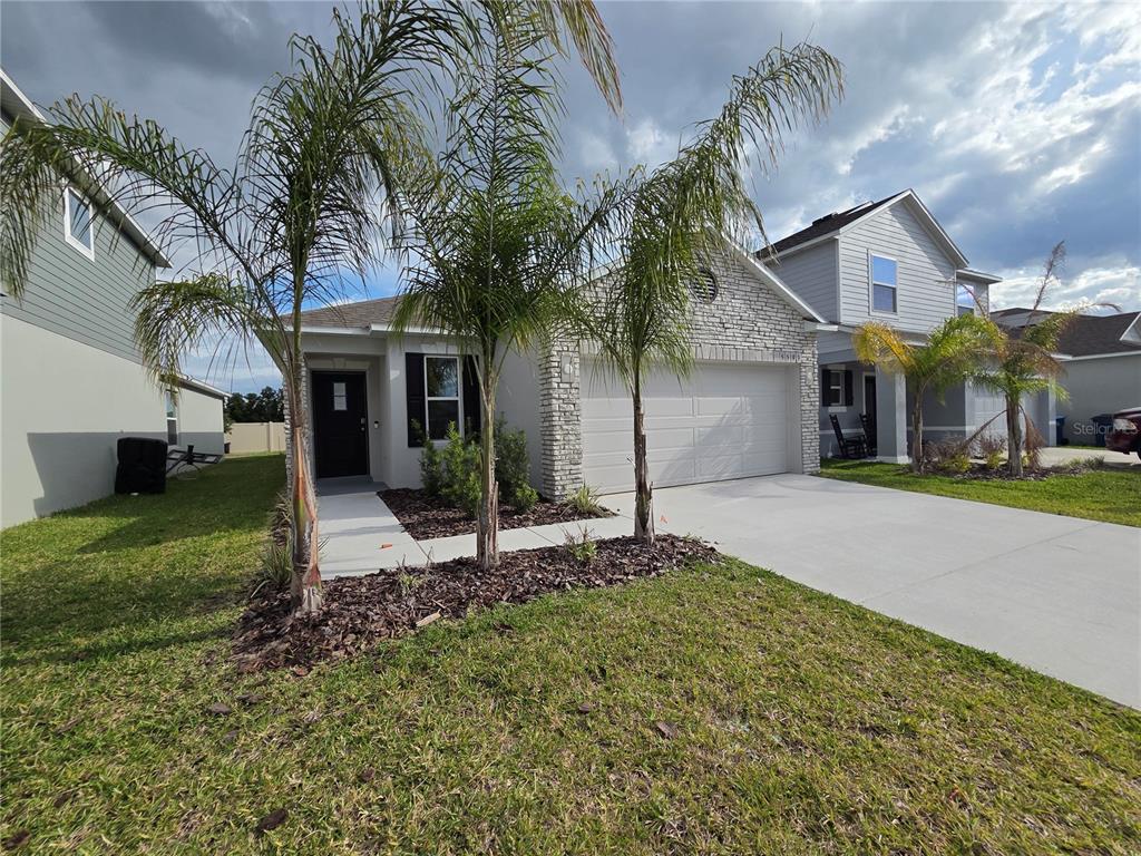A single-story house with a stone facade, two-car garage, and palm trees in the front yard — 5599 MADDIE DRIVE, HAINES CITY, FL