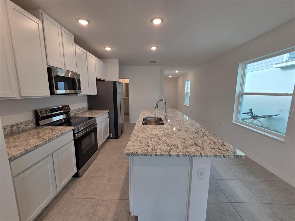 A kitchen features white cabinets, granite countertops, stainless steel appliances, and a large center island — 5599 MADDIE DRIVE, HAINES CITY, FL