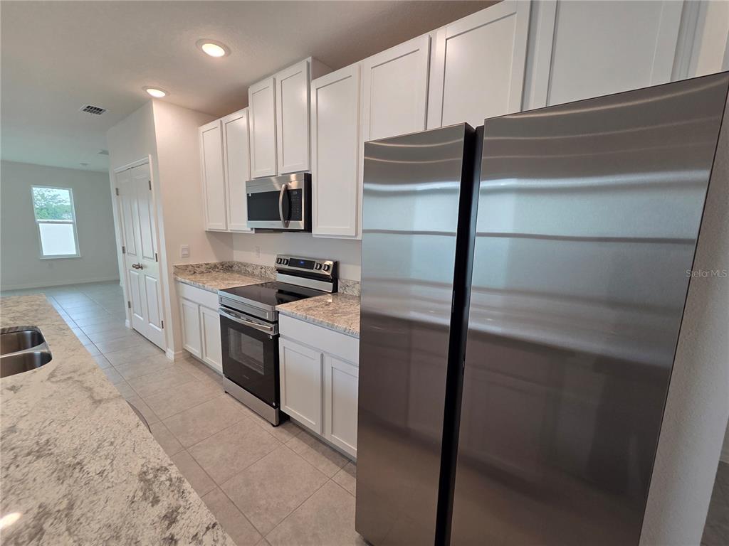 A kitchen features white cabinets, stainless steel appliances, and granite countertops — 5599 MADDIE DRIVE, HAINES CITY, FL
