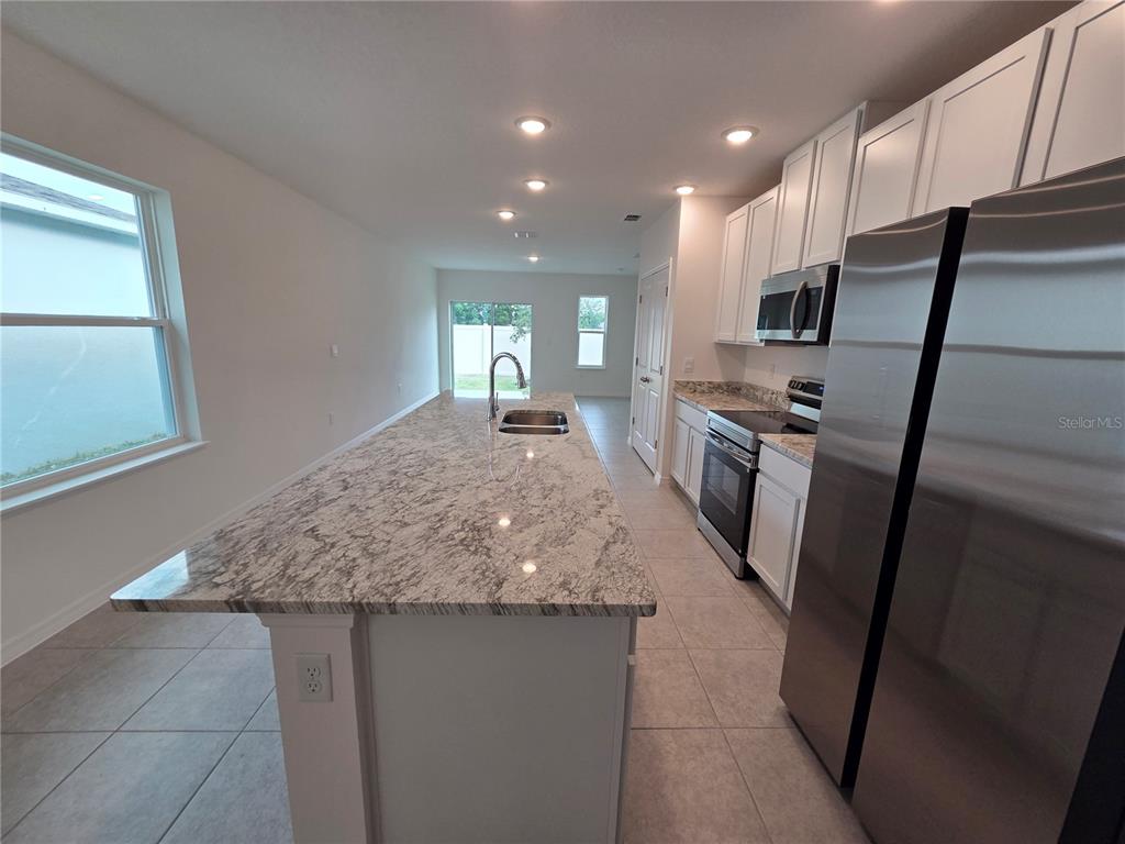 A kitchen features a large granite island, white cabinetry, and stainless steel appliances — 5599 MADDIE DRIVE, HAINES CITY, FL