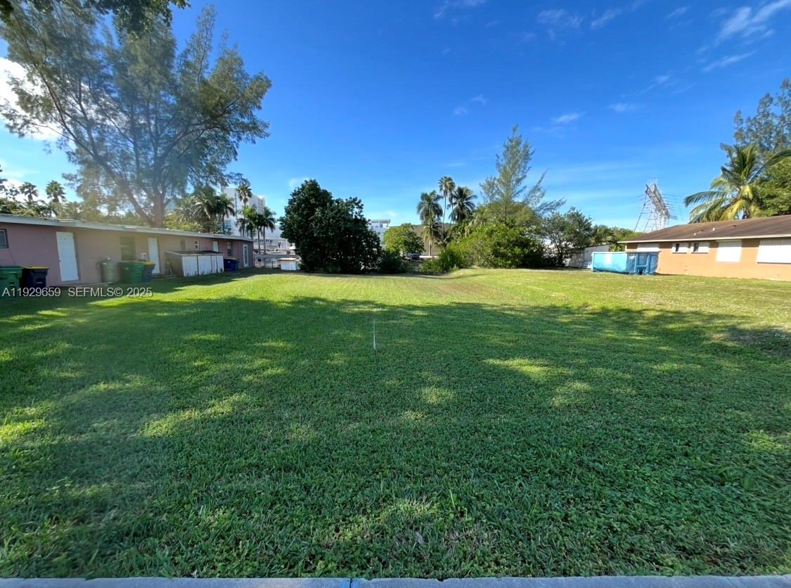 A grassy vacant lot sits between two single-story residential buildings under a clear blue sky — 157 NW 14th Way, Dania Beach FL 33004, DANIA BEACH, FL