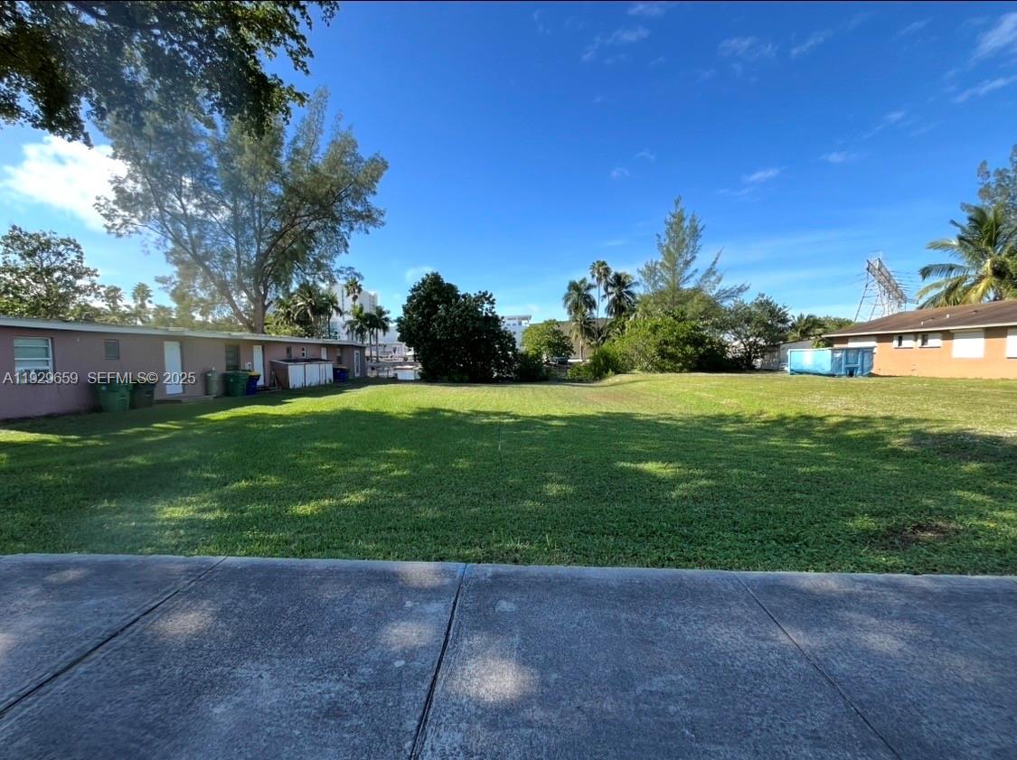 A grassy vacant lot sits between two single-story buildings under a clear blue sky — 157 NW 14th Way, Dania Beach FL 33004, DANIA BEACH, FL