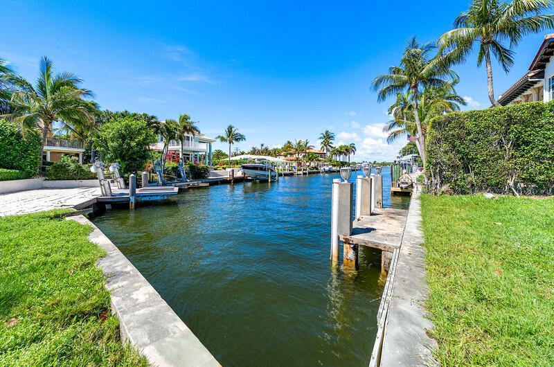 A canal view showing boat docks, palm trees, and waterfront houses under a blue sky — 103 Bonito Drive, Ocean Ridge FL 33435, OCEAN RIDGE, FL