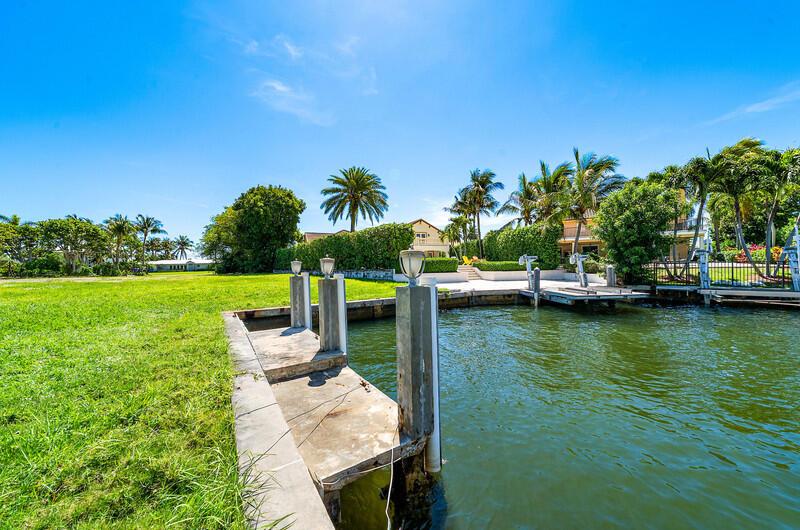 A concrete boat dock extends into a canal next to a grassy lawn and palm trees — 103 Bonito Drive, Ocean Ridge FL 33435, OCEAN RIDGE, FL