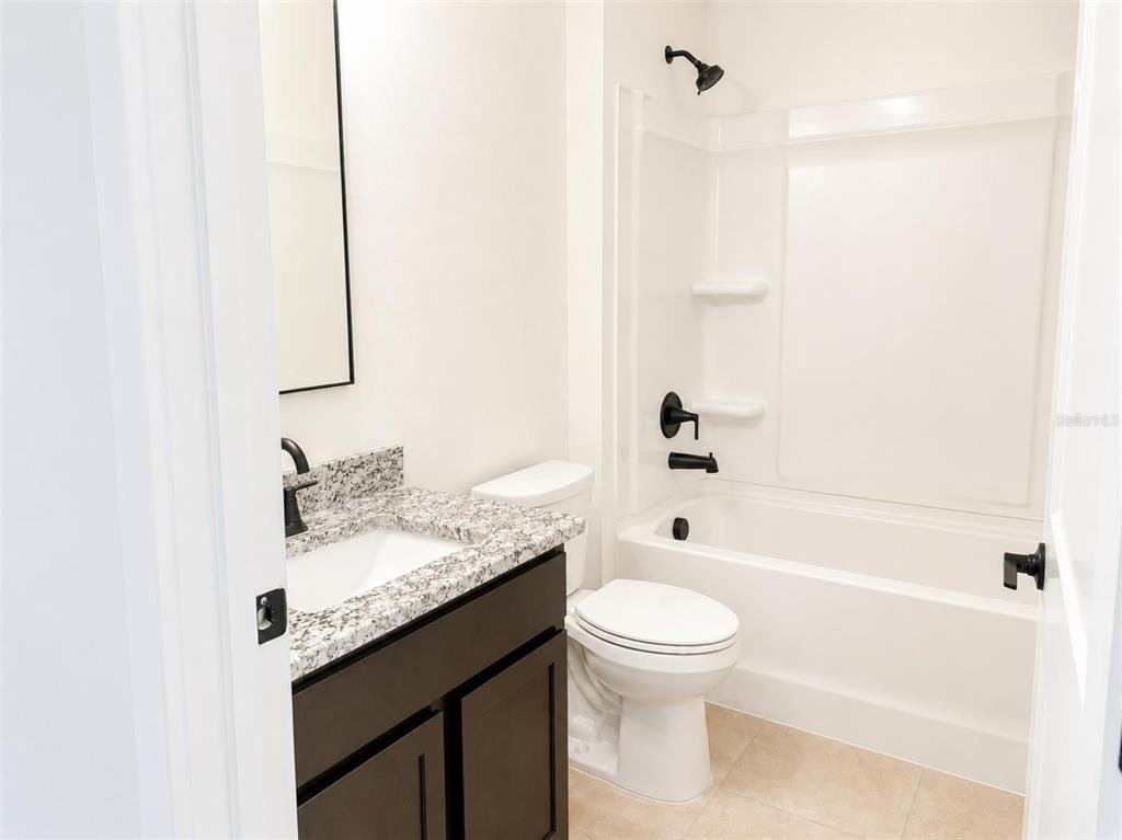 A bathroom features a dark vanity with granite countertop, a toilet, and a tub-shower combo — 247 VERNY GROVE LANE, LEESBURG, FL