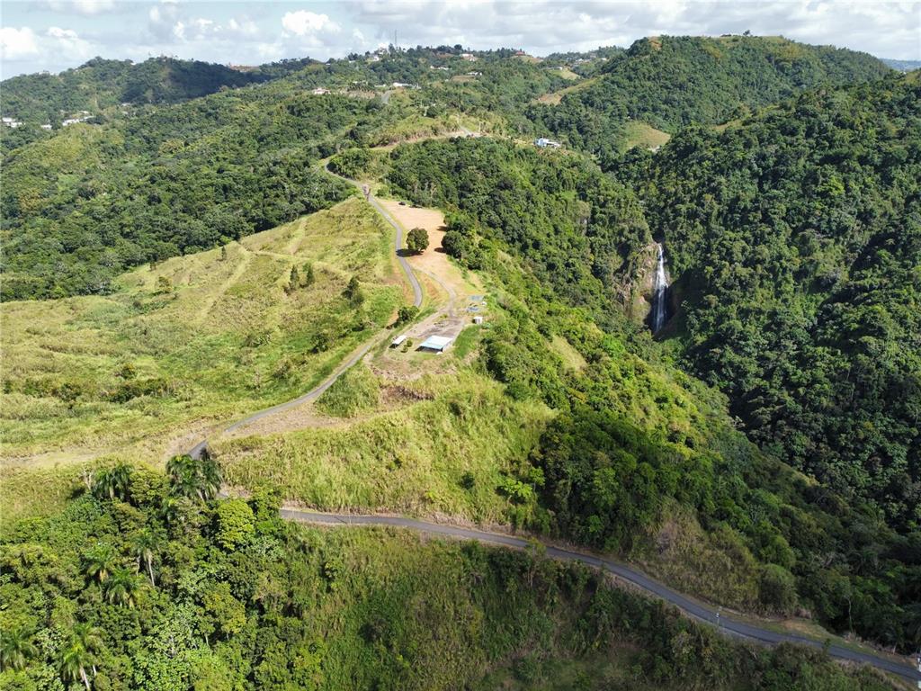 An aerial view shows a winding road leading to a building near a lush waterfall — PR-155 KM 34.0 BARRIO PERCHAS, MOROVIS, PR