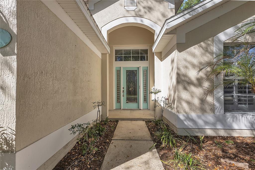 A concrete walkway leads to the front entrance of a house with a teal door — 32 SHINNECOCK DRIVE, PALM COAST, FL
