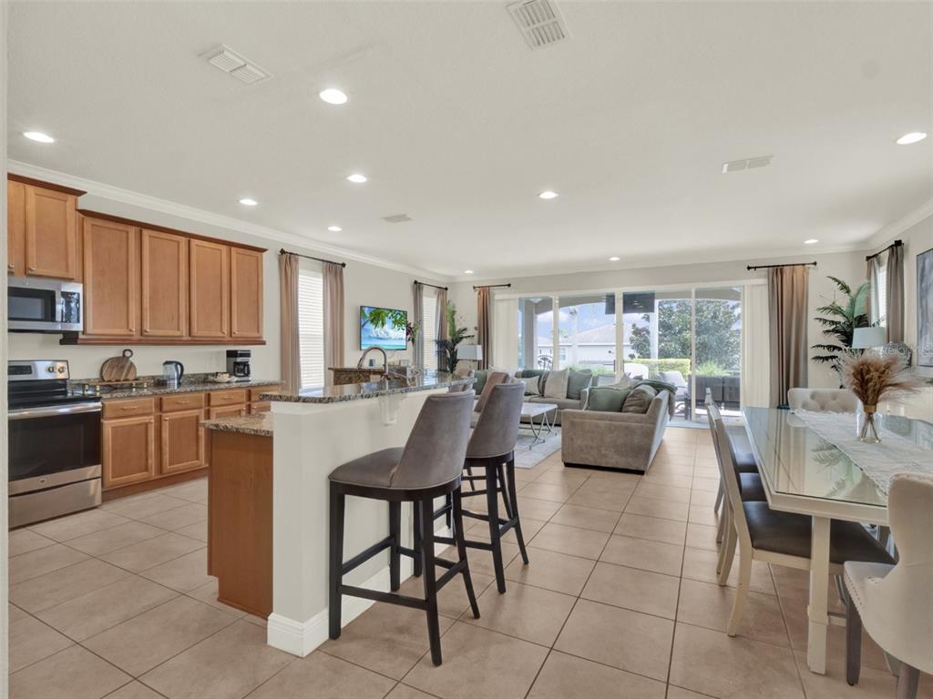 An open-concept kitchen and living area features light wood cabinets, tile floors, and bar seating — 7564 MARKER AVENUE, KISSIMMEE, FL