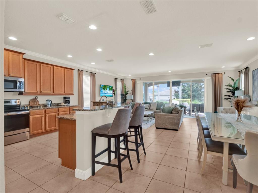 An open-concept kitchen and dining area with light wood cabinets, tile floors, and bar seating — 7564 MARKER AVENUE, KISSIMMEE, FL