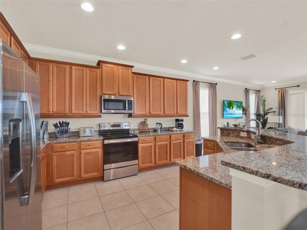 A kitchen features light wood cabinets, granite countertops, stainless steel appliances, and tile flooring — 7564 MARKER AVENUE, KISSIMMEE, FL