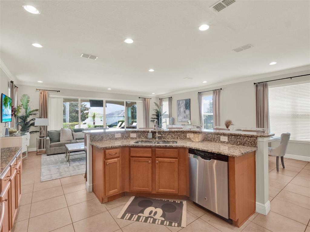 A kitchen with granite countertops and wood cabinets overlooks an open-concept living and dining area — 7564 MARKER AVENUE, KISSIMMEE, FL
