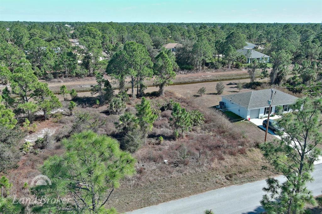 An aerial view shows a vacant, brush-covered lot next to a single-story suburban house — 943 FOXDALE AVENUE, LEHIGH ACRES, FL