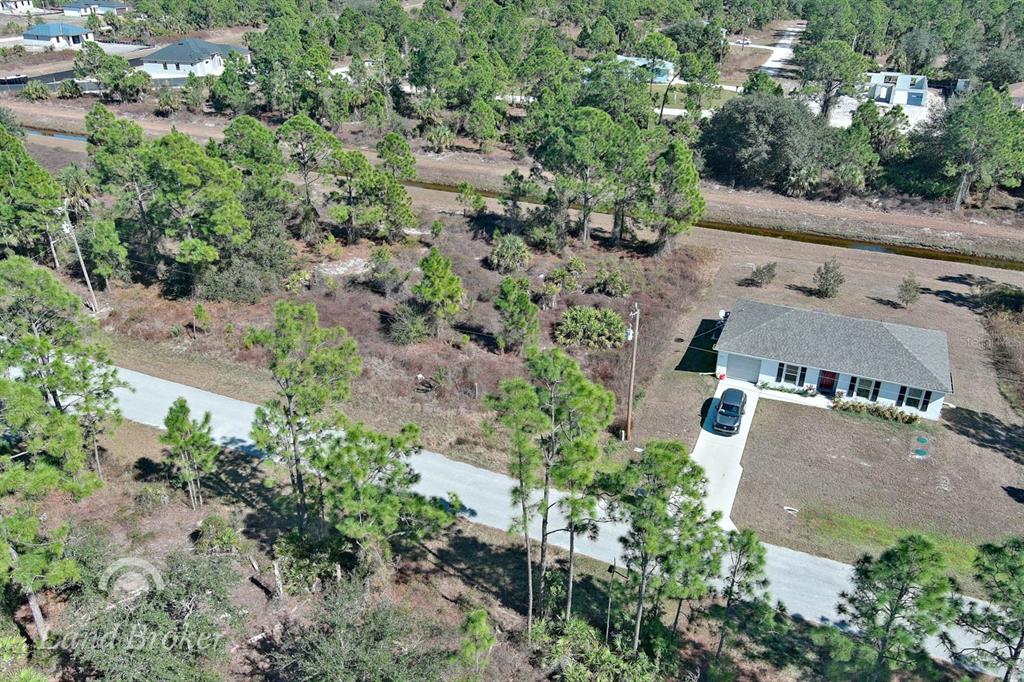 An aerial view shows a single-story house with a driveway next to a wooded lot — 943 FOXDALE AVENUE, LEHIGH ACRES, FL