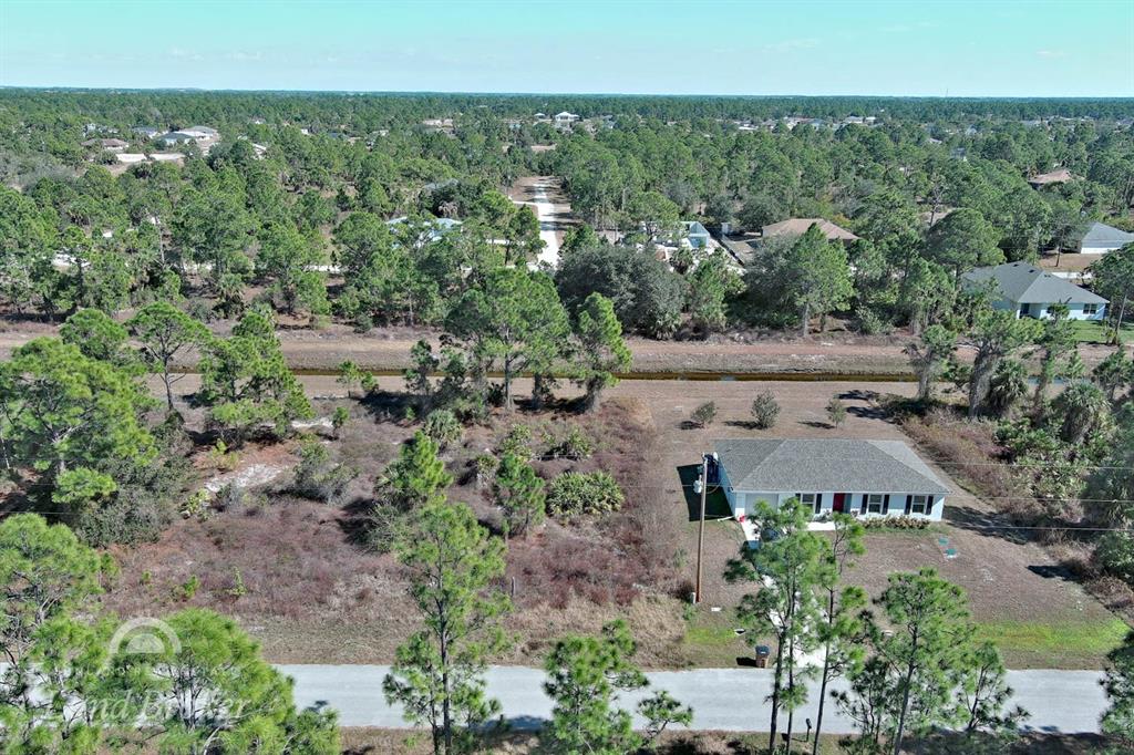 An aerial view shows a single-story house on a large, wooded lot with a canal — 943 FOXDALE AVENUE, LEHIGH ACRES, FL