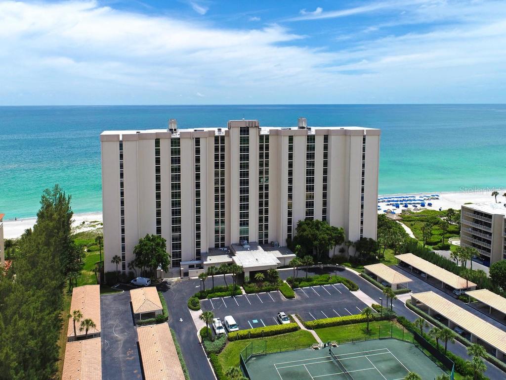 An aerial view of a tall beachfront condominium building with a parking lot and tennis court — 2425 GULF OF MEXICO DRIVE UNIT 7F, LONGBOAT KEY, FL