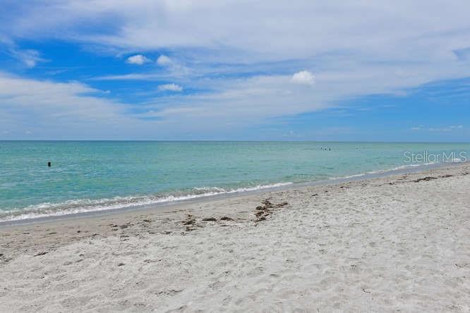 A sandy beach meets the turquoise ocean under a blue sky with scattered white clouds — 2425 GULF OF MEXICO DRIVE UNIT 7F, LONGBOAT KEY, FL