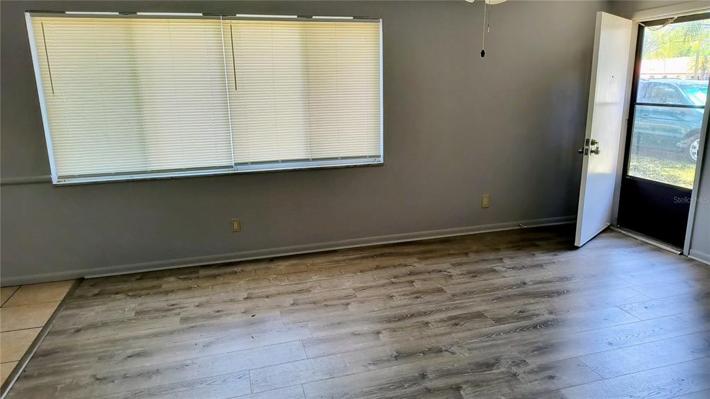 A room with gray walls, wood-look flooring, a large window with blinds, and an open door — 10861 126TH AVENUE, LARGO, FL