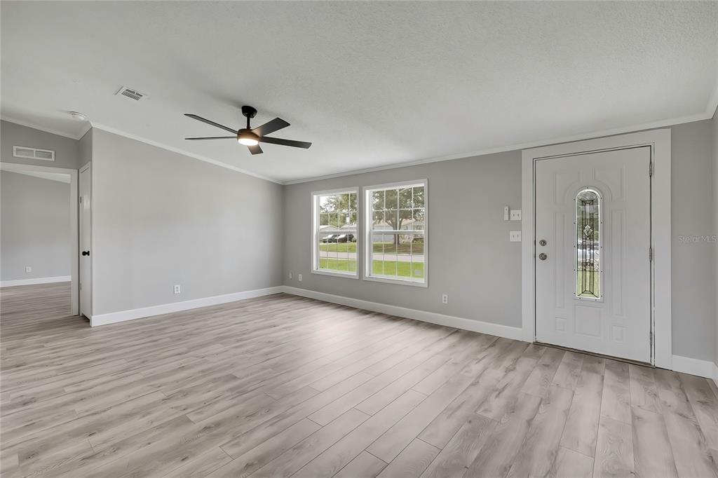 A living room with light gray walls, wood-look flooring, a ceiling fan, and a front door — 36125 WHITE FIR WAY, DADE CITY, FL