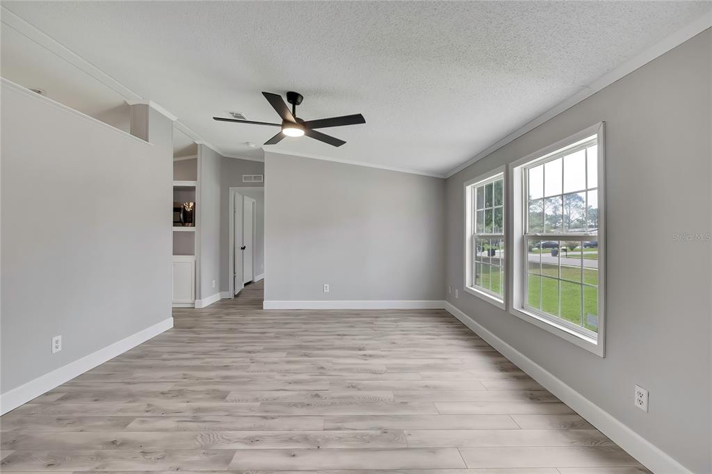 An empty living room features light gray walls, wood-look flooring, a ceiling fan, and two windows — 36125 WHITE FIR WAY, DADE CITY, FL