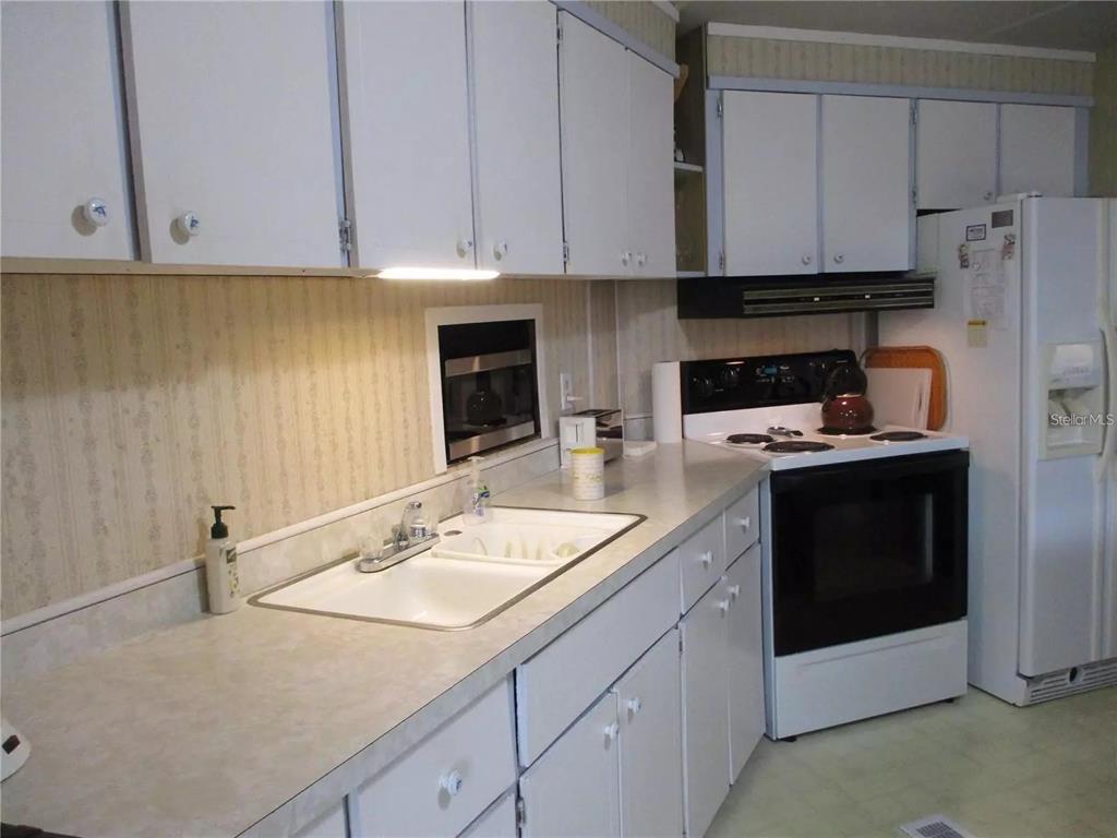 A kitchen features white cabinets, a white double sink, and a white electric range — 4024 REGGIE DR., HOLIDAY, FL