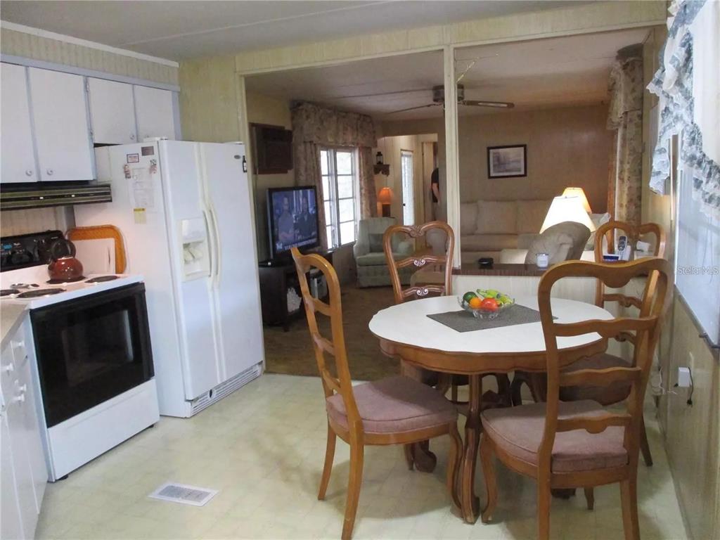 A kitchen with white appliances and cabinets opens into a dining area and living room — 4024 REGGIE DR., HOLIDAY, FL