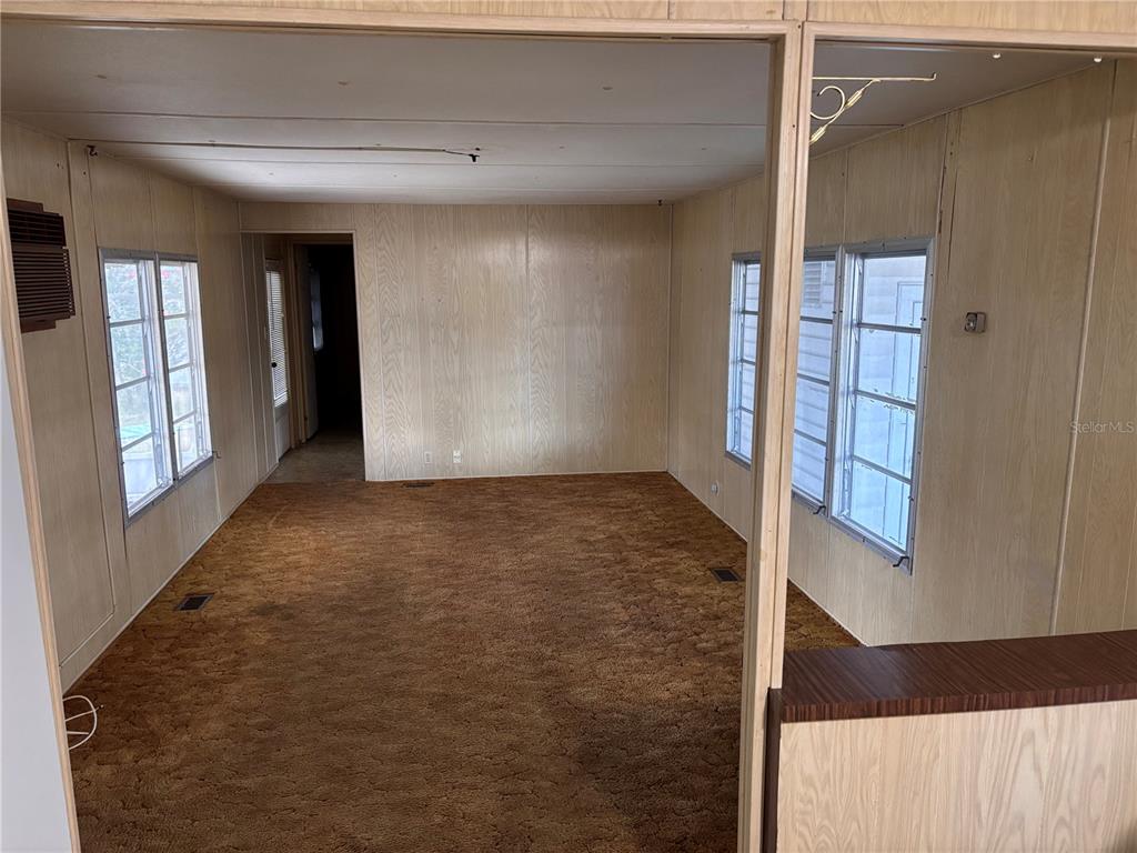 A living room with wood-paneled walls, brown carpeting, and multiple windows — 4024 REGGIE DR., HOLIDAY, FL