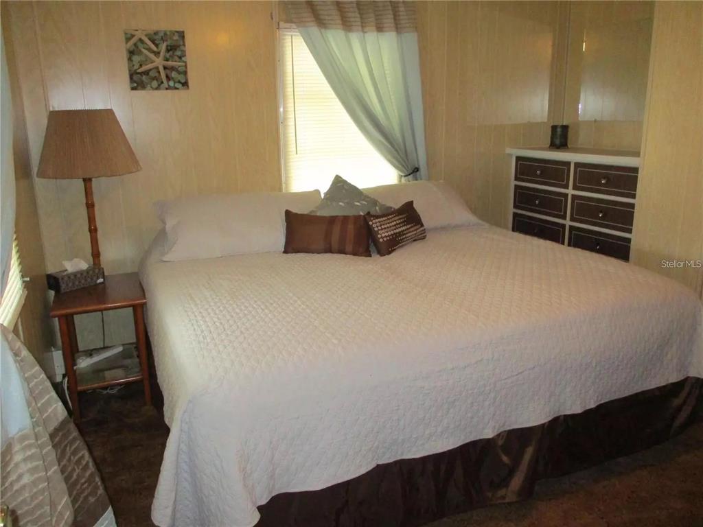 A bedroom features a large bed with a white quilt, wood-paneled walls, and a dresser — 4024 REGGIE DR., HOLIDAY, FL