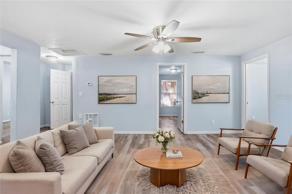 A living room features light blue walls, wood-look flooring, a ceiling fan, and neutral furniture — 2717 13TH AVENUE S, ST PETERSBURG, FL