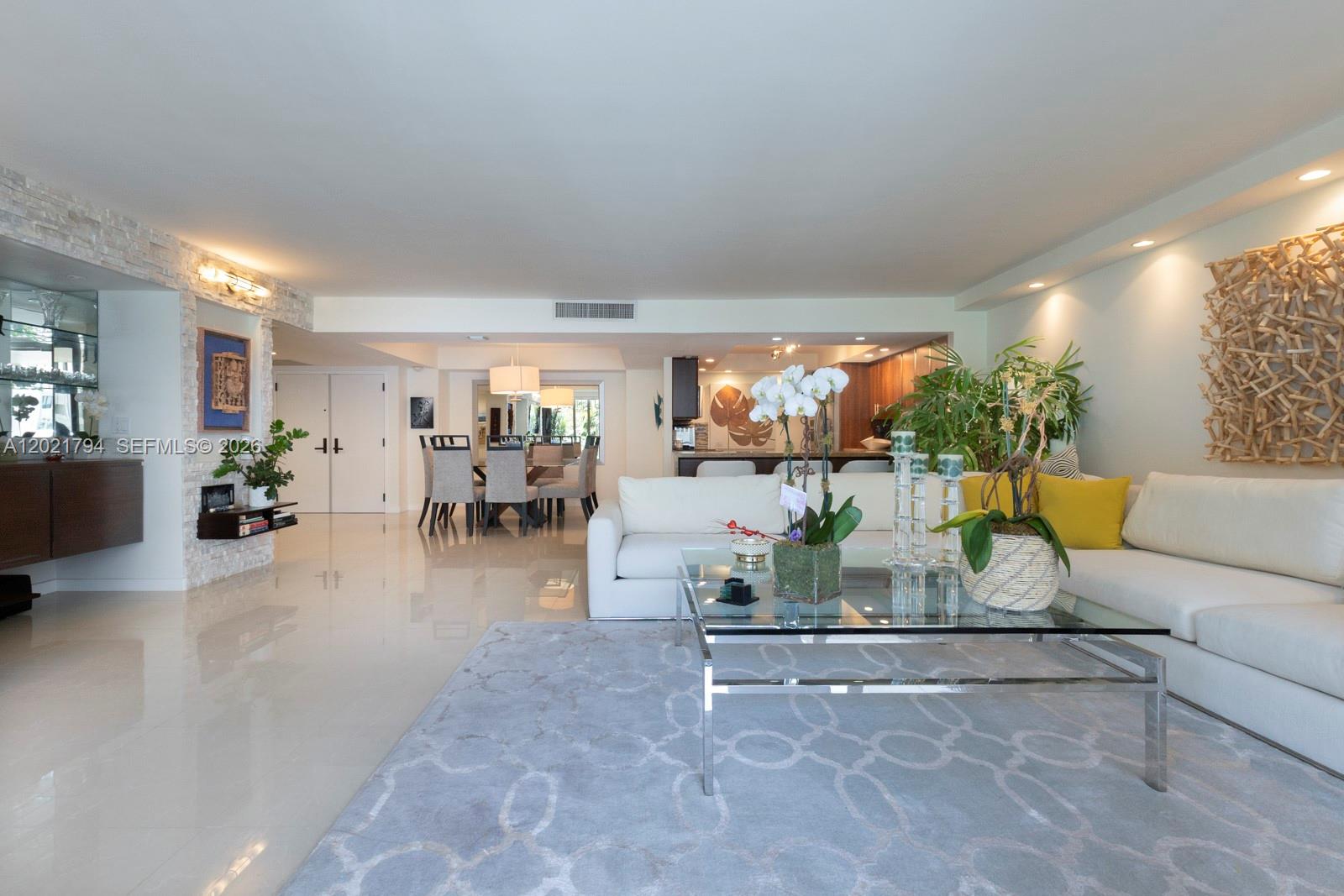 A bright living room features white sofas, a glass coffee table, and a stone accent wall — 3 Grove Isle Dr # C307, Miami FL 33133, MIAMI, FL