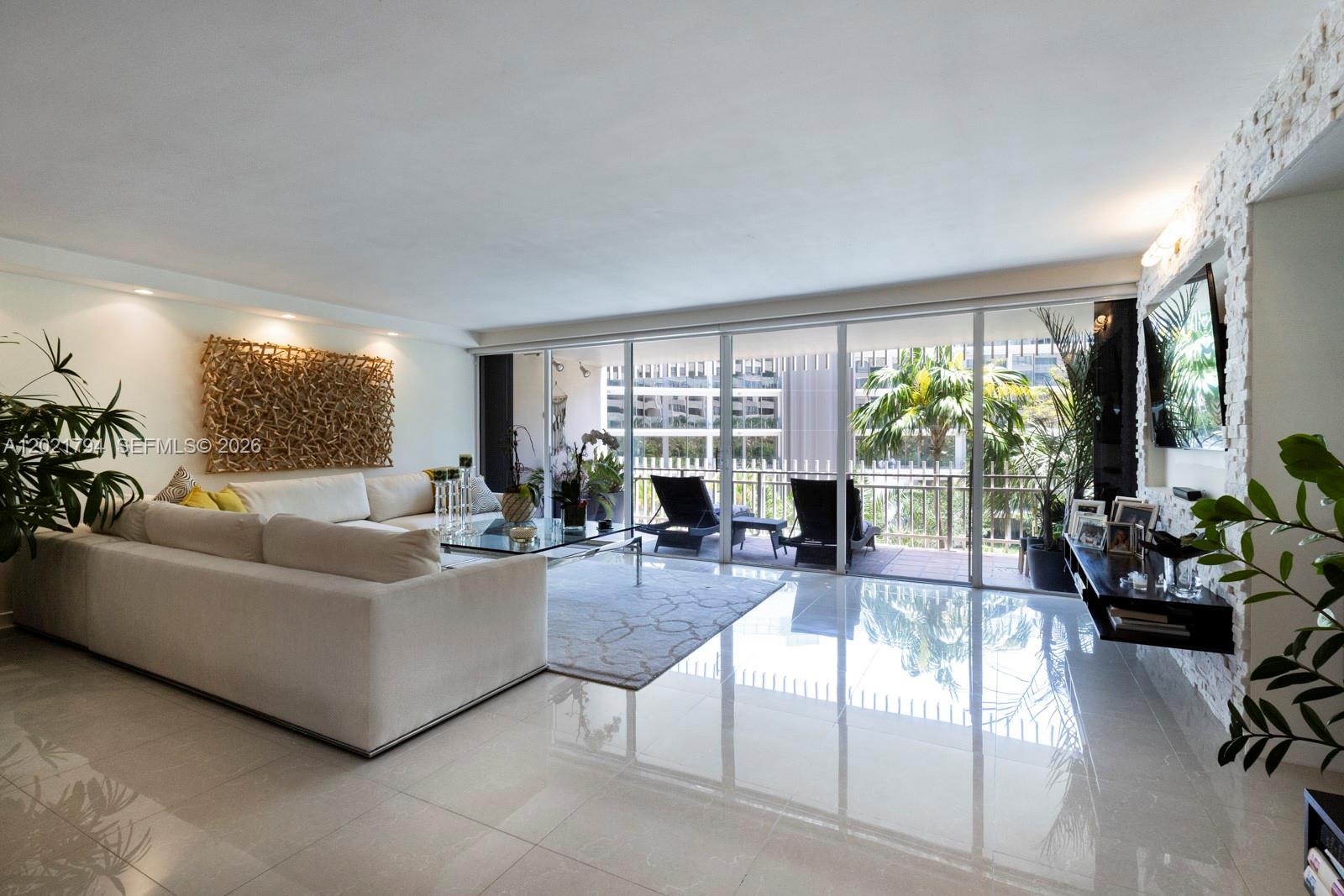A bright living room features white tile floors, a sectional sofa, and a balcony view — 3 Grove Isle Dr # C307, Miami FL 33133, MIAMI, FL