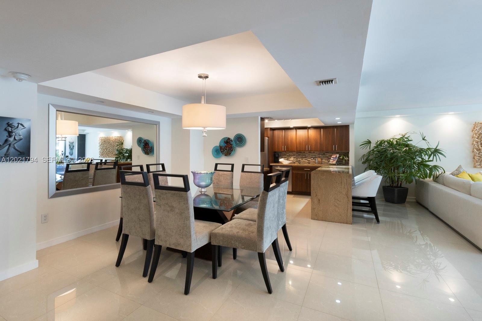 A dining area with a glass table and six chairs sits adjacent to a kitchen — 3 Grove Isle Dr # C307, Miami FL 33133, MIAMI, FL