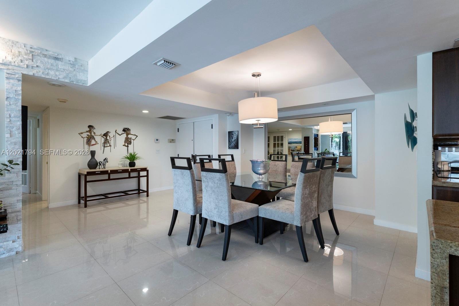 A dining room features a glass-topped table, six upholstered chairs, and a large wall mirror — 3 Grove Isle Dr # C307, Miami FL 33133, MIAMI, FL