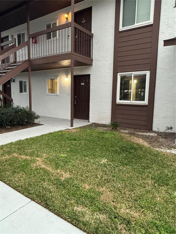A two-story apartment building exterior features brown doors, white stucco walls, and a metal staircase — 39132 COUNTY ROAD 54 UNIT 2018, ZEPHYRHILLS, FL