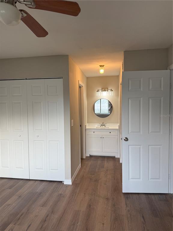 A bedroom features wood-look flooring, a ceiling fan, white closet doors, and an attached vanity — 39132 COUNTY ROAD 54 UNIT 2018, ZEPHYRHILLS, FL