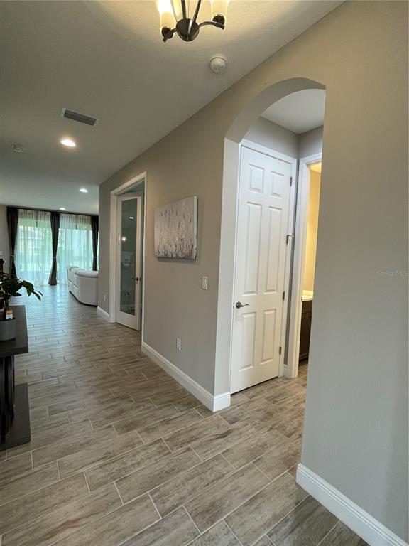 A hallway with wood-look tile flooring leads to a living area and two interior doors — 18036 RAMBLE ON WAY, LAND O LAKES, FL