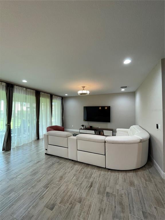 A living room features a large white sectional sofa, a television, and floor-to-ceiling curtains — 18036 RAMBLE ON WAY, LAND O LAKES, FL