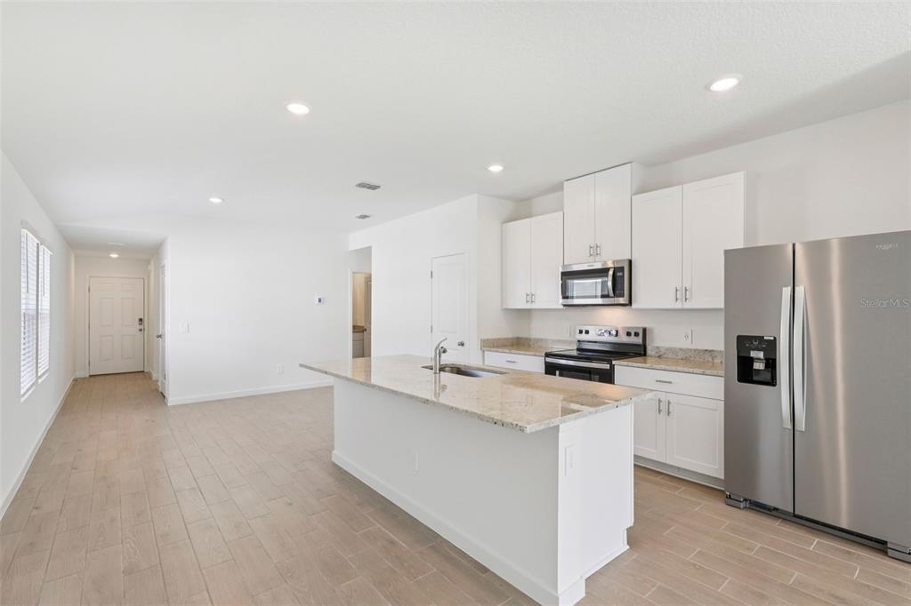 A modern kitchen features white cabinets, granite countertops, stainless steel appliances, and a central island — 16 DERBYSHIRE DRIVE, PALM COAST, FL